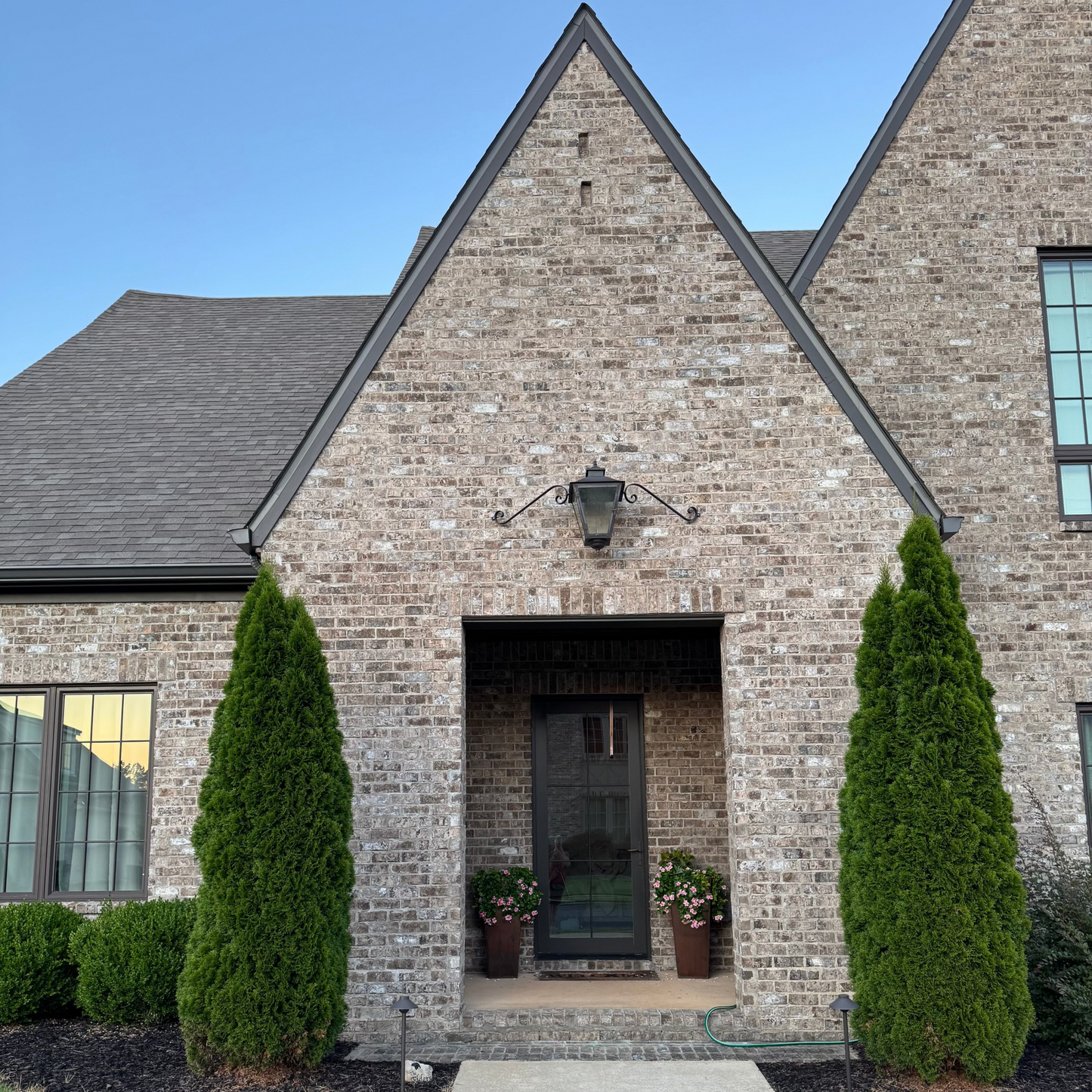 Brick house with a front door and two emerald green thuja framing out the front gable on a clear day