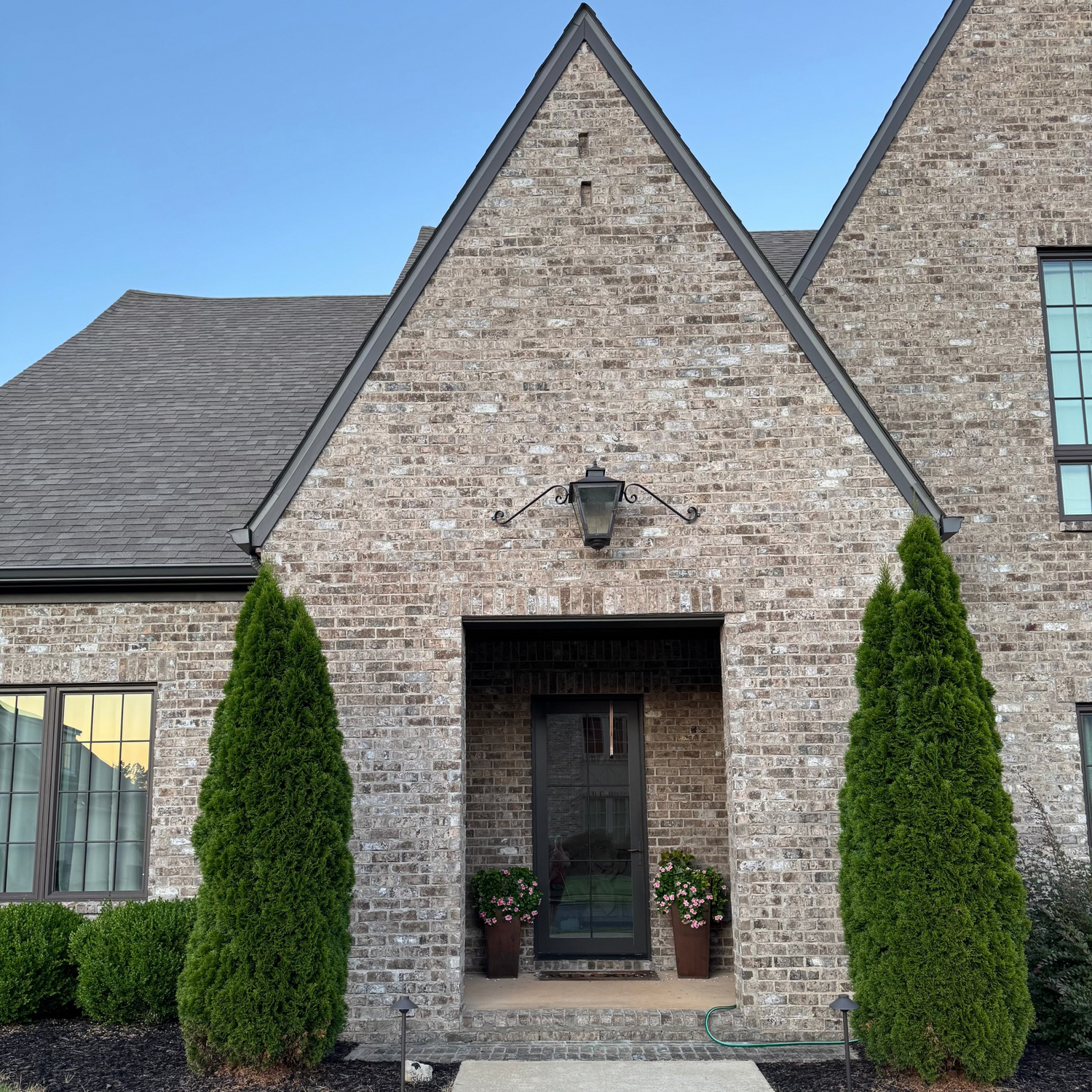 Brick house with a front door and two emerald green thuja framing out the front gable on a clear day